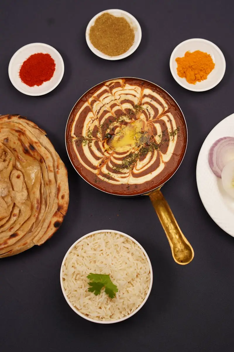 Delicious Indian meal featuring lachha parantha, creamy curry, and assorted spices in a top-down view.